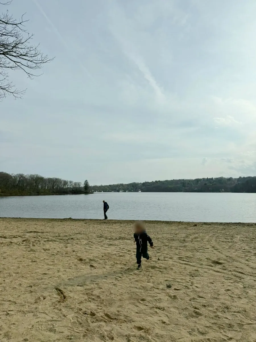 A dad walking along the edge of a lake while his young son runs across the sand toward the camera